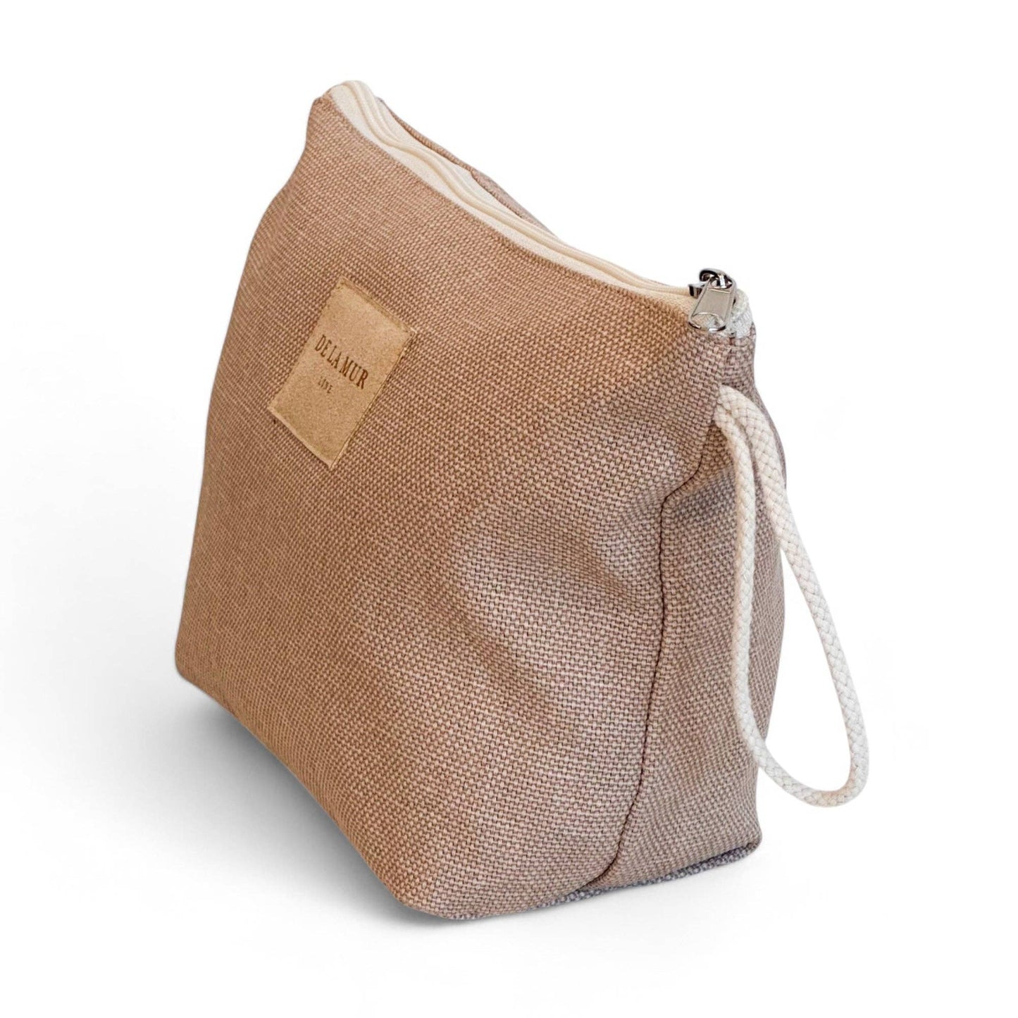 Vista laterale dell’astuccio beige in tessuto spesso con manico in corda color grezzo e chiusura a zip.