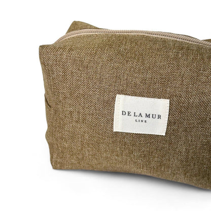 Dettaglio del beauty case ocra in tessuto spesso, con manico laterale e chiusura a zip, ideale come porta trucchi da viaggio.