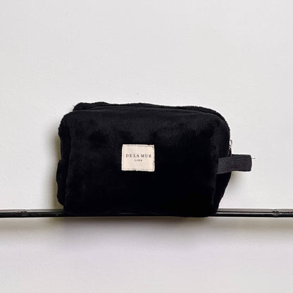 Beauty case in tessuto di pelo morbido nero con cerniera superiore e manico laterale.