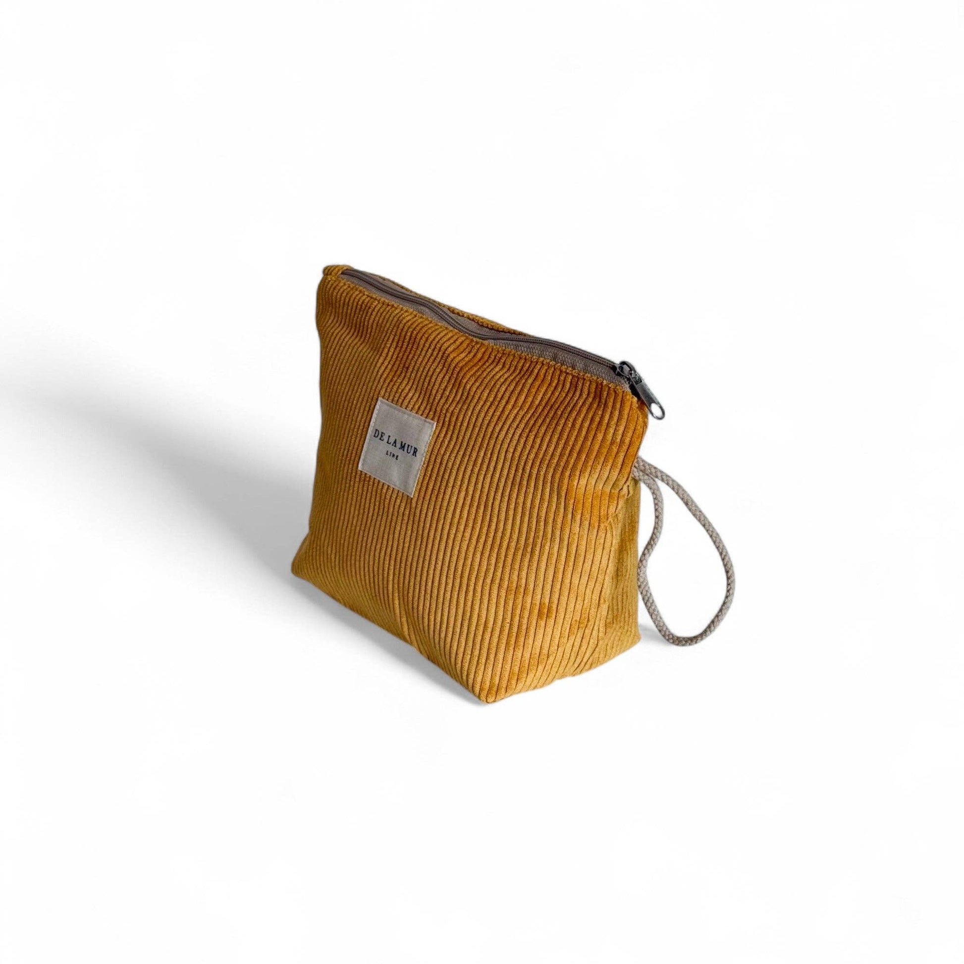 Vista laterale del beauty case in velluto senape con manico in corda beige e chiusura a zip.